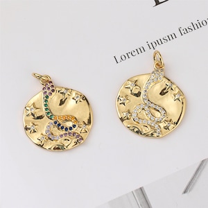 Peut inclure: Deux pendentifs dorés avec un motif de serpent et des accents d'étoiles. Le serpent est incrusté de pierres précieuses colorées.