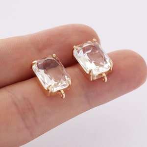 Pode incluir: Dois ajustes de metal dourado com pedras de vidro retangulares transparentes. Cada ajuste tem um pequeno laço na parte inferior.