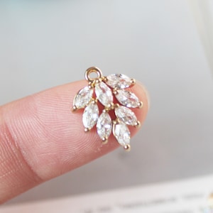 Può includere: Ciondolo dorato con un gruppo di cristalli trasparenti a forma di marquise. Il ciondolo è progettato per assomigliare a una foglia o un ramo.