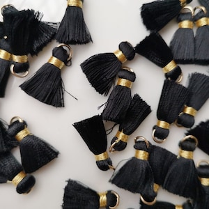 May include: A collection of black tassel trim with gold accents. The tassels are made of soft, silky fabric and have a delicate fringe. They are perfect for adding a touch of elegance to any project.