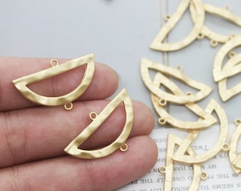 Op de afbeelding: Gouden metalen halve cirkelvormige bedels met een gehamerde textuur en drie springringen. De bedels zijn gerangschikt op een hand en een wit oppervlak.