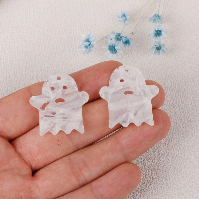 Puede incluir: Dos abalorios de acr&iacute;lico de forma de fantasma blancos con un patr&oacute;n de remolino. Los abalorios tienen un agujero en la parte superior para colgar.