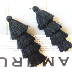 May include: A pair of black tassel earrings with three layers of fringe. The tassels are made of a soft, silky material.