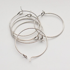 May include: Five silver hoop earrings with a simple, circular design. The hoops are all the same size and are made of a thin, wire-like material.