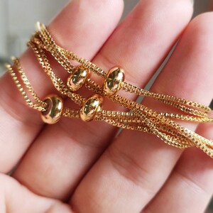 May include: A gold chain bracelet with multiple strands and round beads. The bracelet is made of a delicate chain and has a simple, elegant design.