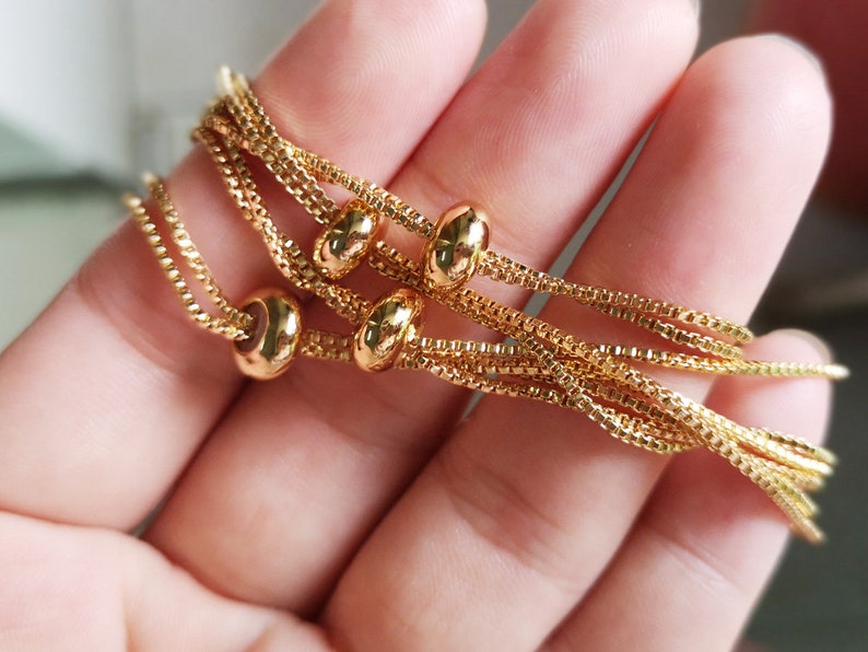 May include: A gold chain bracelet with multiple strands and round beads. The bracelet is made of a delicate chain and has a simple, elegant design.