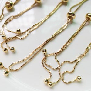 May include: Four gold chain bracelets with adjustable sliding knots and multiple round beads. The bracelets are layered on a white surface.