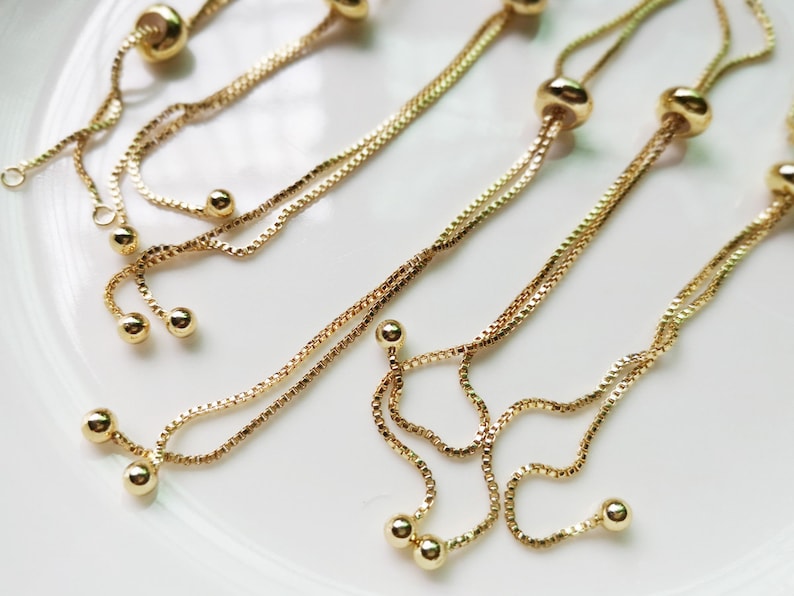 May include: Four gold chain bracelets with adjustable sliding knots and multiple round beads. The bracelets are layered on a white surface.