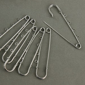 May include: A set of six silver safety pins, each with five loops. The pins are arranged in a fan shape.