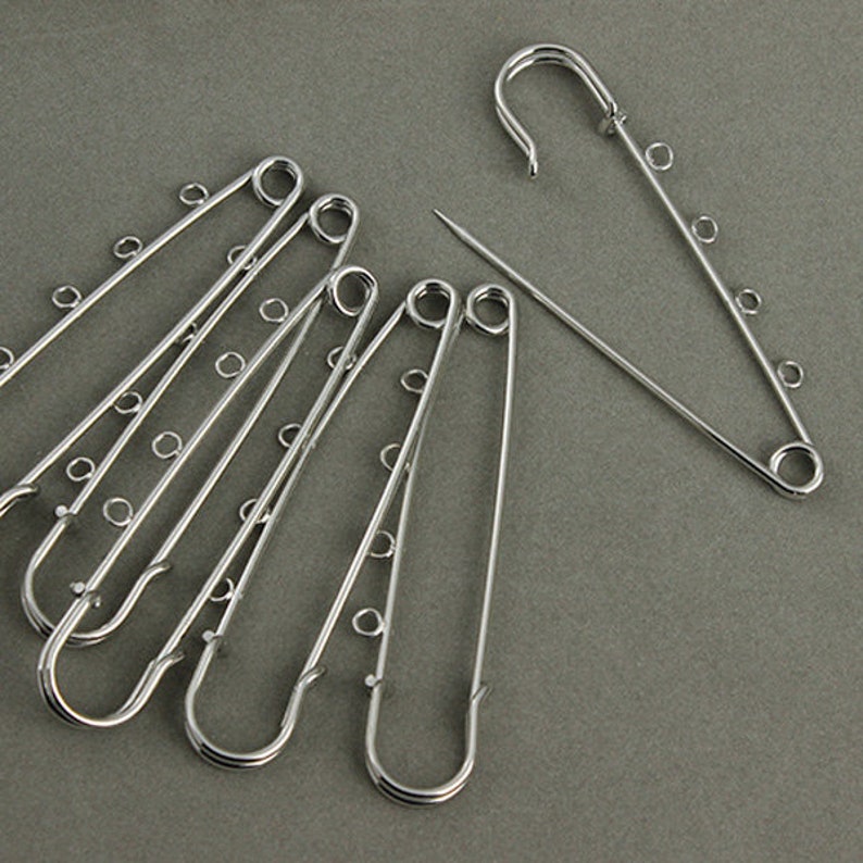May include: A set of six silver safety pins, each with five loops. The pins are arranged in a fan shape.