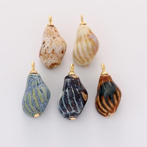 Op de afbeelding: Vijf keramische hangers in verschillende kleuren, waaronder beige, blauw, bruin en crème. Elke hanger heeft een goudkleurige beugel aan de bovenkant. De hangers hebben een druppelvorm met een getextureerd oppervlak.