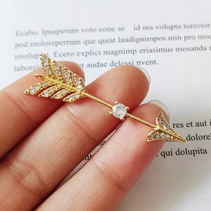 May include: A gold arrow charm with clear crystal accents. The arrow is adorned with small, sparkling crystals that create a dazzling effect.