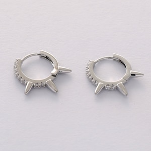 May include: A pair of silver hoop earrings with small spikes and clear cubic zirconia stones.