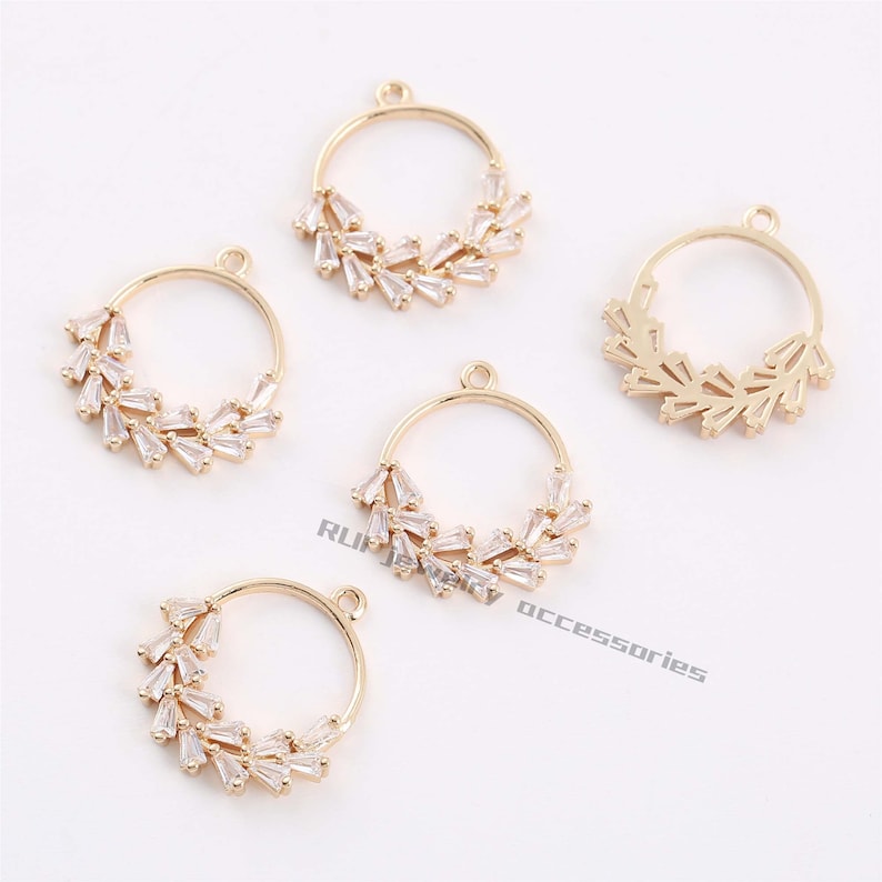 May include: Five gold-toned metal circle pendant charms with clear crystal accents. The charms are designed with a circle frame and a row of crystal accents around the perimeter.