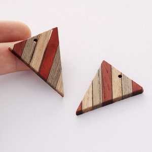 May include: Two wooden triangle shaped pendants with a hole in the top. The wood is a mix of brown, red, and white stripes.