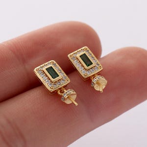 May include: Gold-tone earring with a square-shaped pendant featuring a green emerald-like stone surrounded by clear cubic zirconia stones. The pendant is attached to a gold-tone post.