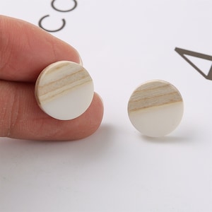 May include: A pair of round wooden earrings with a white and natural wood finish.