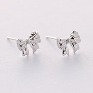 May include: A pair of silver bow-shaped stud earrings.