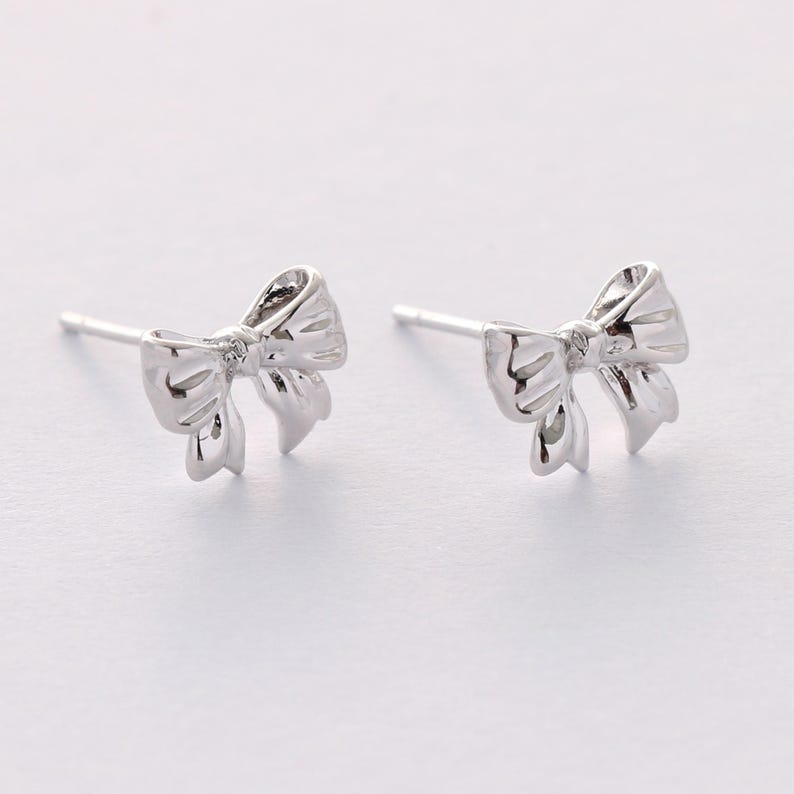 May include: A pair of silver bow-shaped stud earrings.