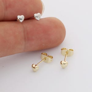 Può includere: Un paio di piccoli orecchini a lobo a forma di cuore color argento e un paio di piccoli orecchini a lobo a forma di cuore color oro con chiusure a farfalla in metallo abbinate. Gli orecchini presentano una finitura liscia e lucida.