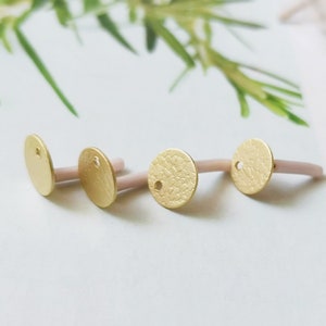 Könnte beinhalten: Drei goldfarbene Metallkreise mit einem Loch in der Mitte. Die Kreise haben eine strukturierte Oberfläche und sind an einem weißen, flexiblen Material befestigt.
