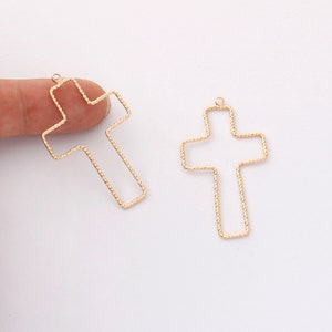 May include: Two gold-toned metal cross shapes with a textured wire design. The crosses are open and have a loop at the top for hanging.