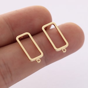 May include: Two gold-toned rectangular earring blanks with a small loop at the bottom. The blanks are open on all sides.