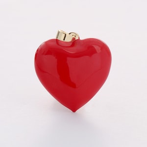 May include: A red heart-shaped pendant with a gold bail. The pendant is made of a smooth, shiny material.