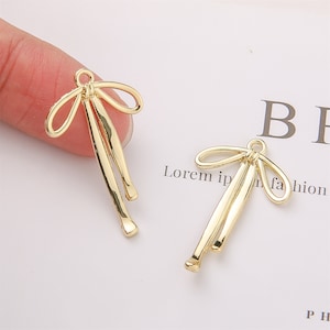 May include: Two gold-toned metal bow charms with a loop at the top. The bows are made of thin wire and have a delicate, feminine look.