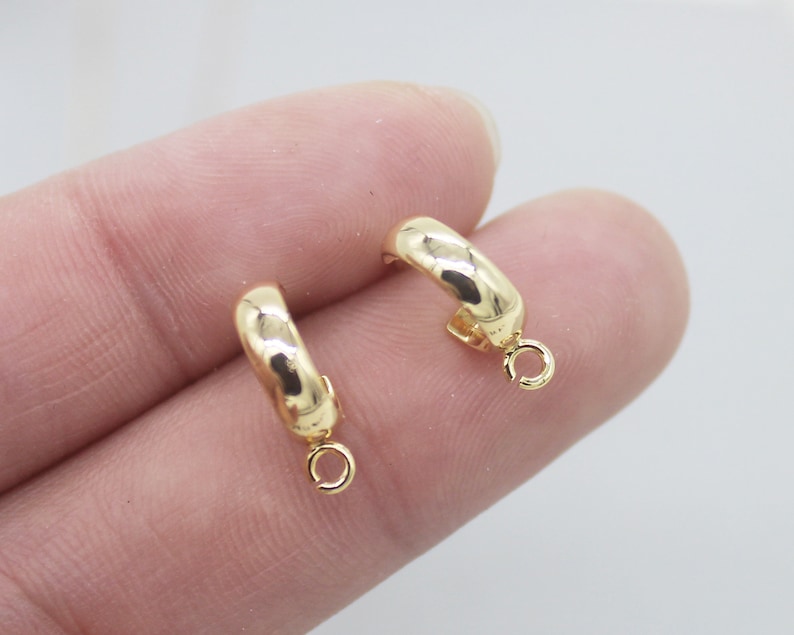 May include: Two gold-toned hoop earrings with a small jump ring hanging from each hoop.