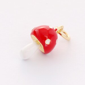 May include: A red and white enamel mushroom charm with a gold-tone finish. The charm has a white stem and a red cap with white polka dots.