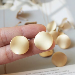 Peut inclure: Une paire de boucles d'oreilles rondes, légèrement incurvées, de couleur or. Les boucles d'oreilles sont lisses et ont une finition mate.