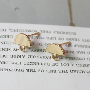 May include: Two gold-toned half-circle earring findings with jump rings. The findings are on a white surface.