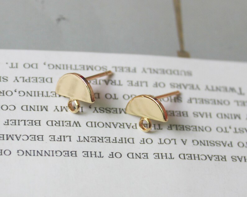 May include: Two gold-toned half-circle earring findings with jump rings. The findings are on a white surface.