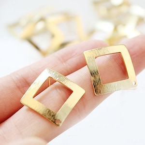 May include: Two gold-toned square-shaped earring blanks with a brushed finish. The blanks have a hole at the top for attaching earring wires.