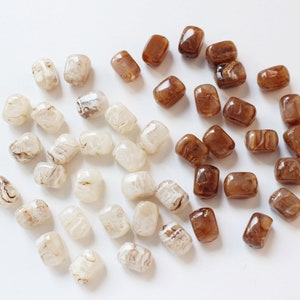 May include: A collection of brown and white agate beads. The beads are rectangular and have a swirling pattern.