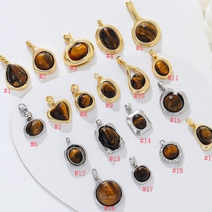 May include: A selection of pendant necklaces with diverse shapes and designs. The pendants display polished tiger's eye stones set in gold and silver-toned metal. The collection includes heart, oval, and teardrop shapes.