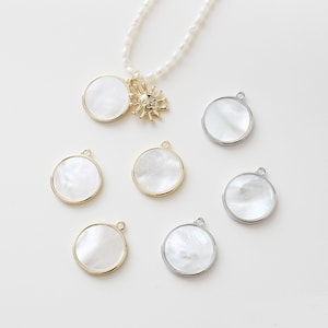 May include: A set of seven round, white mother-of-pearl pendants with gold and silver trim. The pendants are strung on a pearl necklace with a sun charm.
