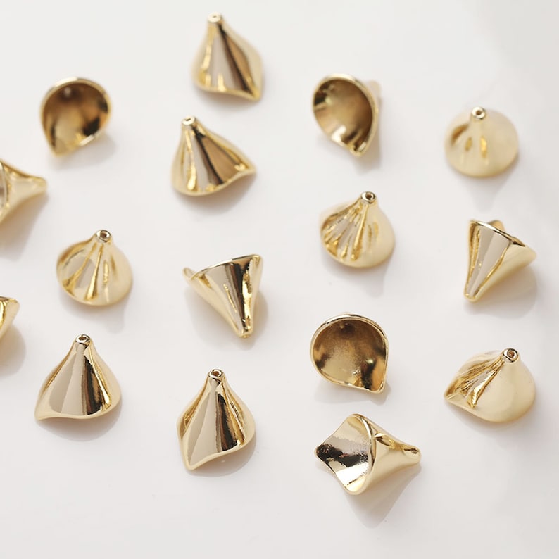 Peut inclure: Un ensemble de 15 perles en m&eacute;tal de couleur dor&eacute;e en forme de c&ocirc;ne. Les perles ont une surface textur&eacute;e et sont dispos&eacute;es sur un fond blanc.