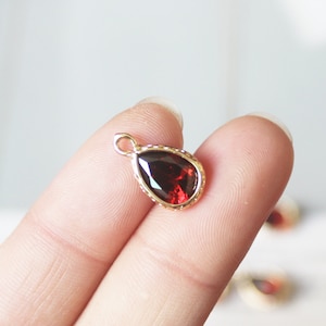 May include: A gold pendant with a red teardrop-shaped gemstone. The pendant has a detailed, textured edge.