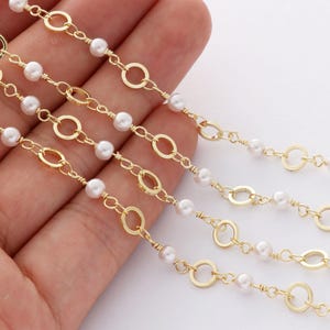 May include: Five strands of gold chain with small white pearls. The chain has a delicate, open circle design.