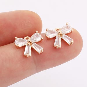 May include: Two gold-tone bow-shaped charms with clear crystal accents. Each charm has a loop for attaching to jewelry or other crafts.