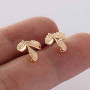 May include: A pair of gold-toned leaf-shaped earrings. The earrings are small and delicate, with a simple design.