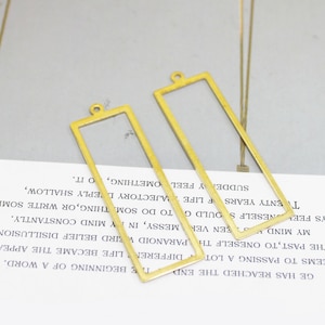 Könnte beinhalten: Zwei goldfarbene rechteckige Metallrahmen mit einer Öse oben. Die Rahmen sind leer und bereit für die individuelle Gestaltung.