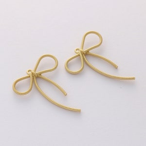 May include: Two gold-colored metal bow charms with a loop at the top for attaching to jewelry or other crafts.