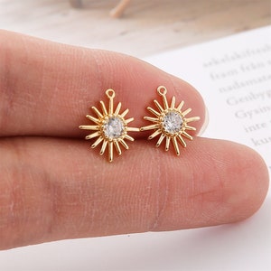 May include: Two gold-tone sun charm pendants with a clear rhinestone in the center. Each charm has a loop at the top for attaching to jewelry.