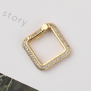 May include: Gold-toned square-shaped clasp with a clear crystal embellishment around the perimeter.
