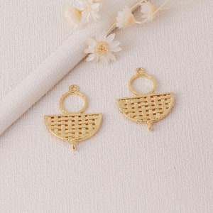 May include: Two gold-colored earring pendants. Each pendant features a woven, semi-circular design with a small loop at the top and a small hook at the bottom. A small circular loop is attached above the semi-circle. The earrings are on a white surface.