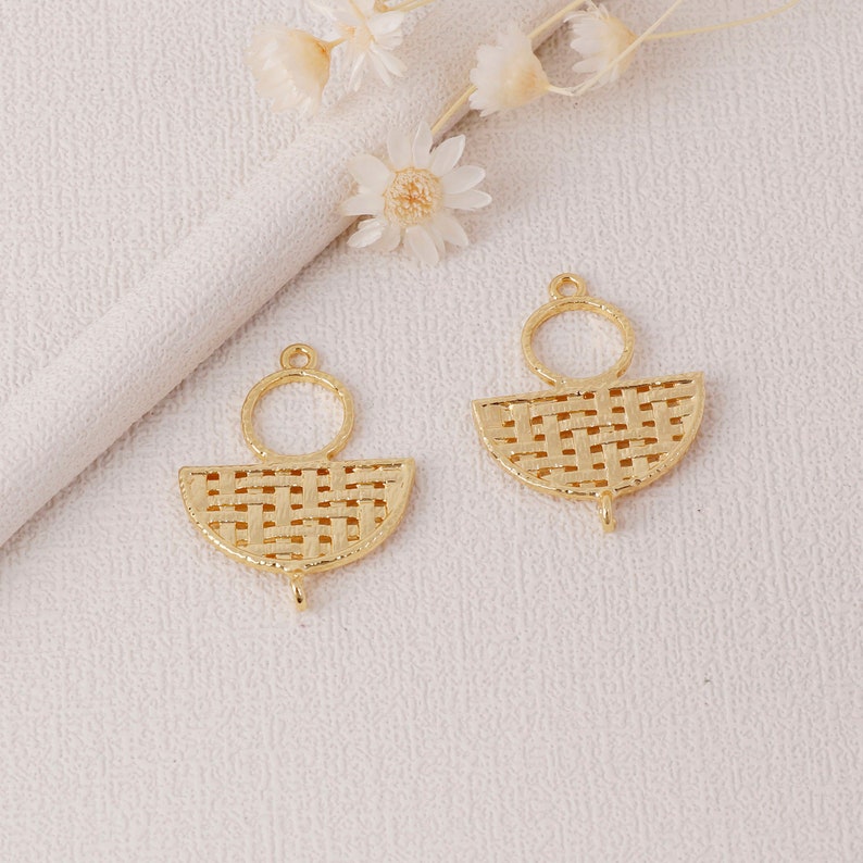 May include: Two gold-colored earring pendants. Each pendant features a woven, semi-circular design with a small loop at the top and a small hook at the bottom. A small circular loop is attached above the semi-circle. The earrings are on a white surface.