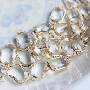 Puede incluir: Primer plano de una cadena de cuentas facetadas de vidrio transparente con conectores de metal dorado. Las cuentas están dispuestas en forma escalonada y tienen un ligero brillo iridiscente.